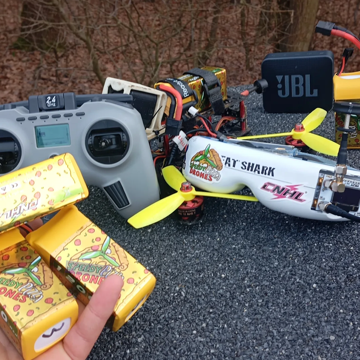 FPV drone setup with radio transmitter and CNHL LiPo batteries laid out on the ground before a flight session