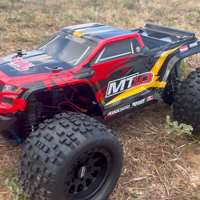 Team Associated RIVAL MT10 1/10 Scale 3S Monster Truck parked on grass, showing V2 red body and stock off-road tires