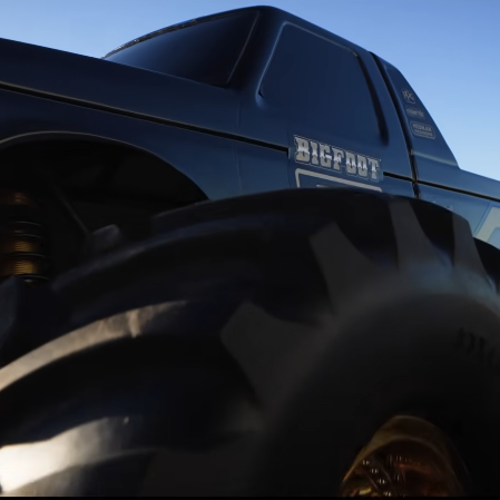 Traxxas X Monster BIGFOOT 50th limited edition monster truck close-up showcasing tire tread and black-and-gold body under sunlight