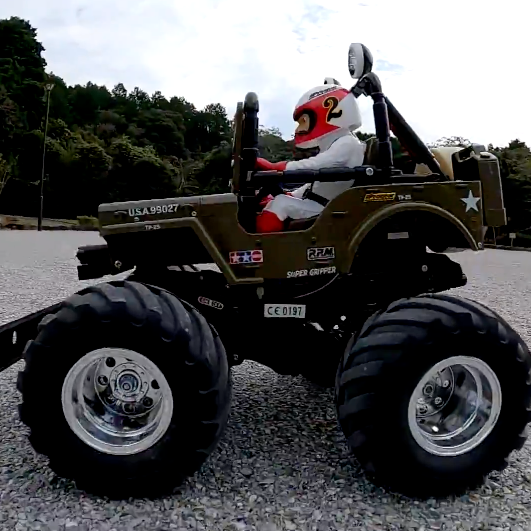 Tamiya Wild Willy 2 WR-02 driving on gravel with driver figure, showcasing off-road stance and oversized tires