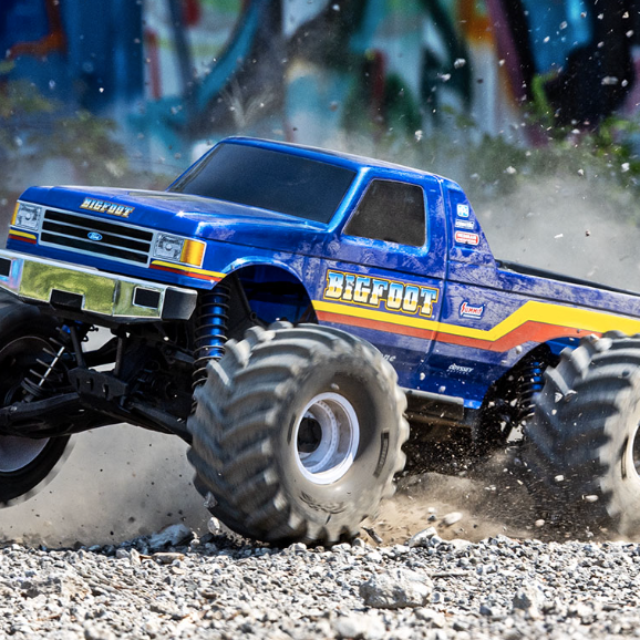 Traxxas X-Monster RC truck with Bigfoot body tearing through dirt, showing massive tires and 8S LiPo power